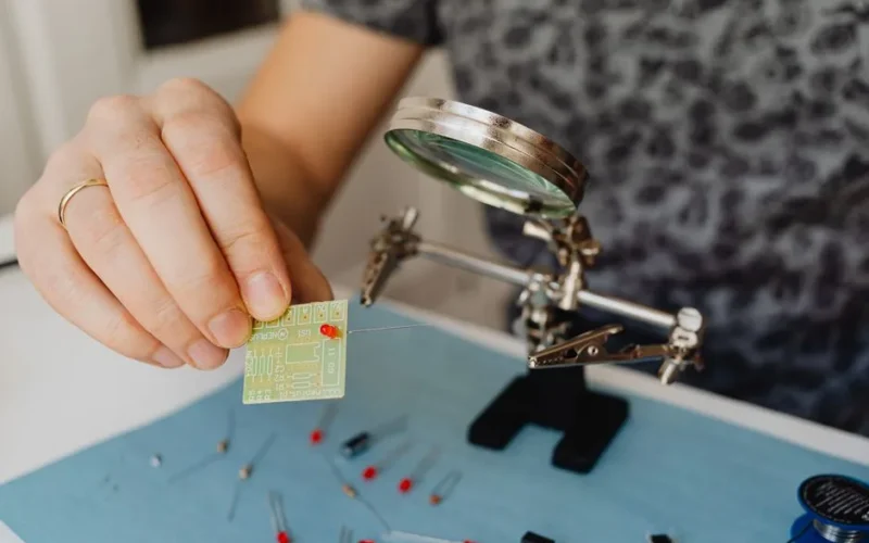 Detailed view of a technician repairing a circuit board using a magnifying glass.