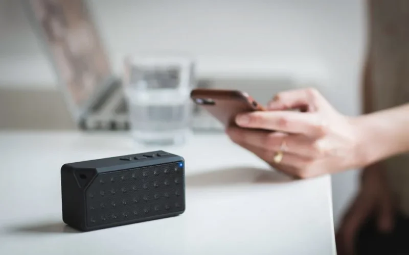 Person connecting a smartphone to a wireless speaker indoors, foreground focus.