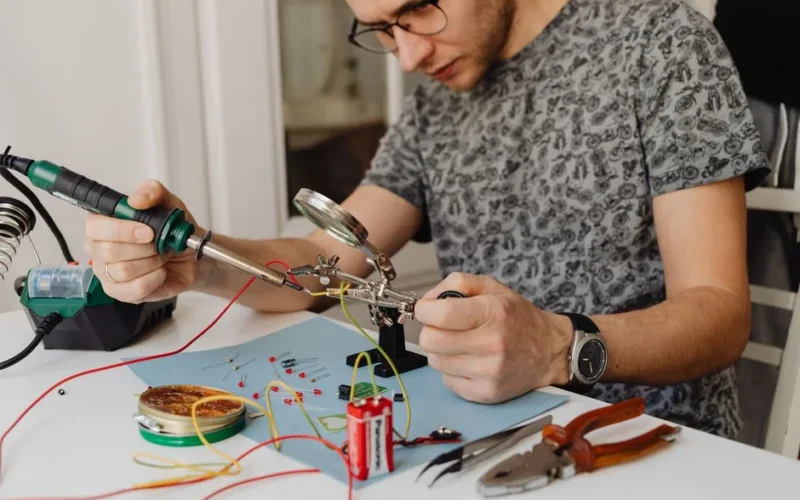 Adult technician soldering electronics with precision tools and equipment indoors.