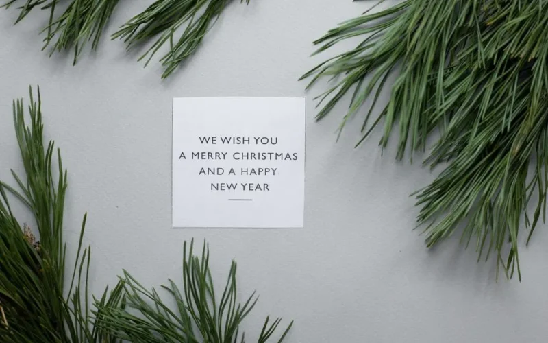 Top view of card with We Wish You A Merry Christmas phrase placed on gray background with green spruce twigs
